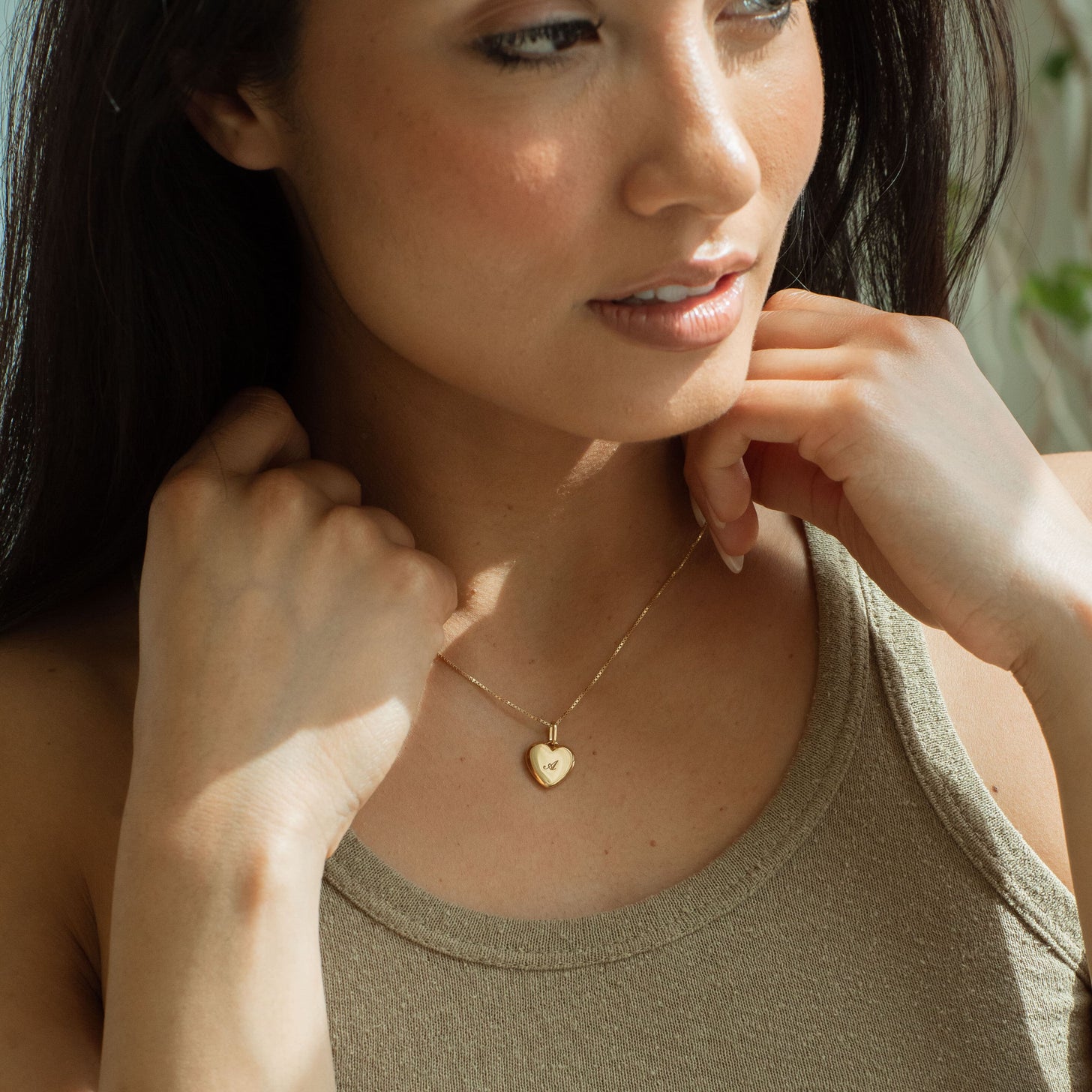 Model wears a gold heart necklace with engraved letters on front and back